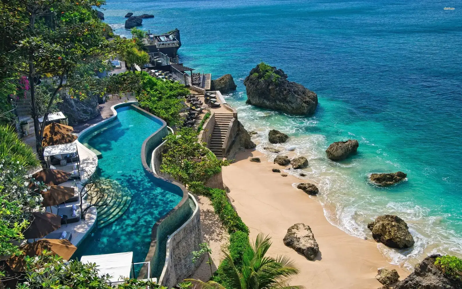 Aerial view of Bali's coastline with a cliffside pool and beach